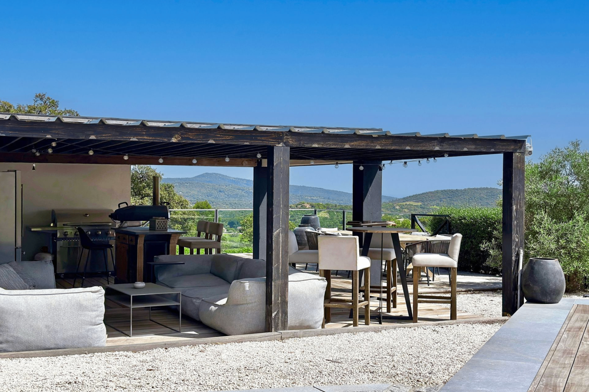 Terrasse pool house — pergola, salons lounge, bar et cuisine d'été face aux collines